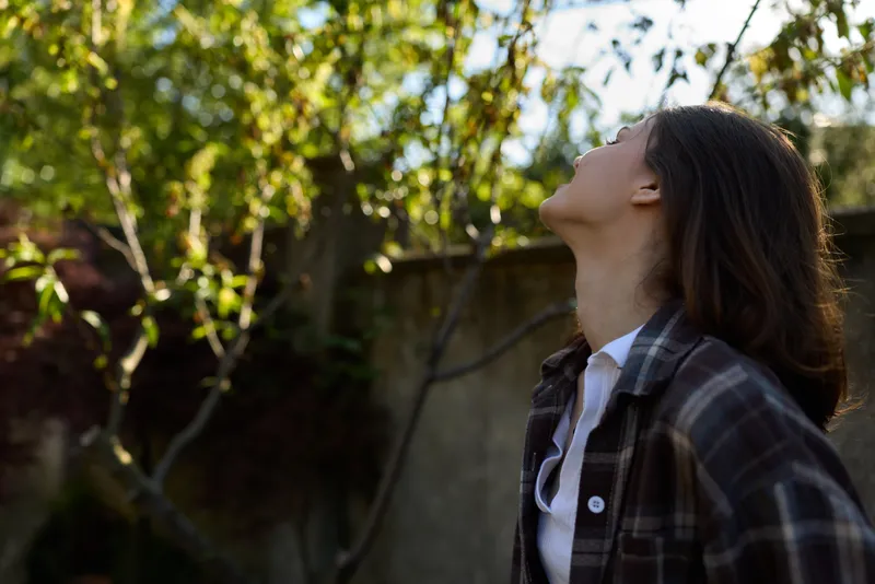 Portrait of a woman lifestyle in a sunny garden, wearing a plaid jacket and white shirt, calm expression, natural light, outdoor scene, relaxed posture, authentic everyday moment
