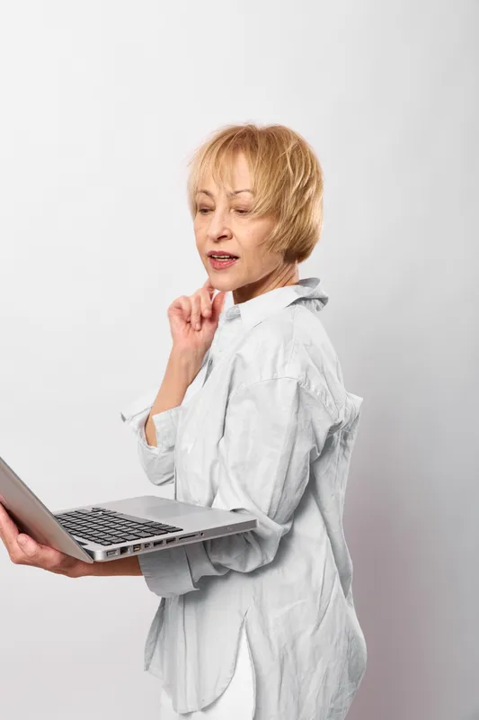 Senior woman doctor in white coat, holding laptop, hand on neck, worried face, throat pain, stress, healthcare and telemedicine concept, bright studio background
