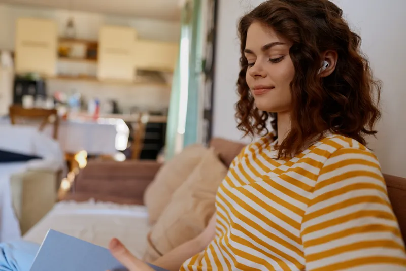 Woman reading in a cozy home, bright striped shirt, warm natural light, relaxed mood, everyday lifestyle, comfortable setting, calm and inviting atmosphere.