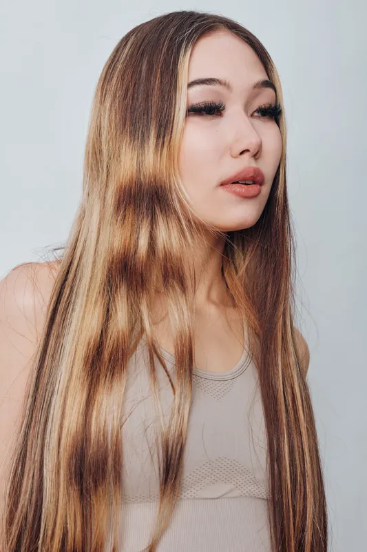 Young woman with long straight hair and natural makeup, wearing a sleeveless top, posing on neutral background with soft lighting and calm expression.