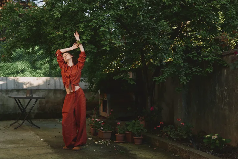 Vibrant woman in a red outfit dancing outdoors in a lush garden, capturing a candid moment of motion and freedom. Expressive lifestyle, wellness vibe, warm natural light, serene mood
