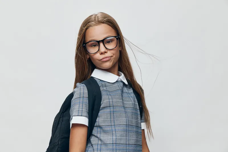 Girl with glasses and long hair wearing school uniform and backpack isolated on white background. Portrait of confident student ready for education and learning at school or academy.
