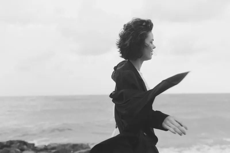 Woman running along a windy beach, motion captured by the shoreline in black and white, conveying freedom and movement by the sea.