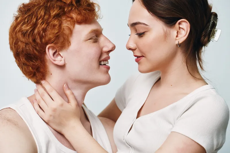 Couple in intimate moment with woman holding man neck, closeup of young woman and man looking at each other with affection on neutral background.