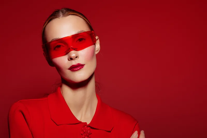 Portrait of a stylish woman wearing red sunglasses and a red outfit against a red background. Concept of fashion, modern style, and bold color contrast in studio lighting.
