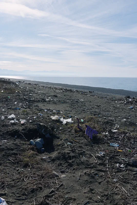 Beach litter and debris along a dark rocky shore, polluted coastline with scattered trash and waste by the sea, a stark view of environmental neglect