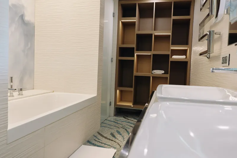 Bathroom scene with a modern tub, white sink, and open storage shelves. Clean lines, neutral tones, and tiled floor create a calm, organized space ideal for daily routines.