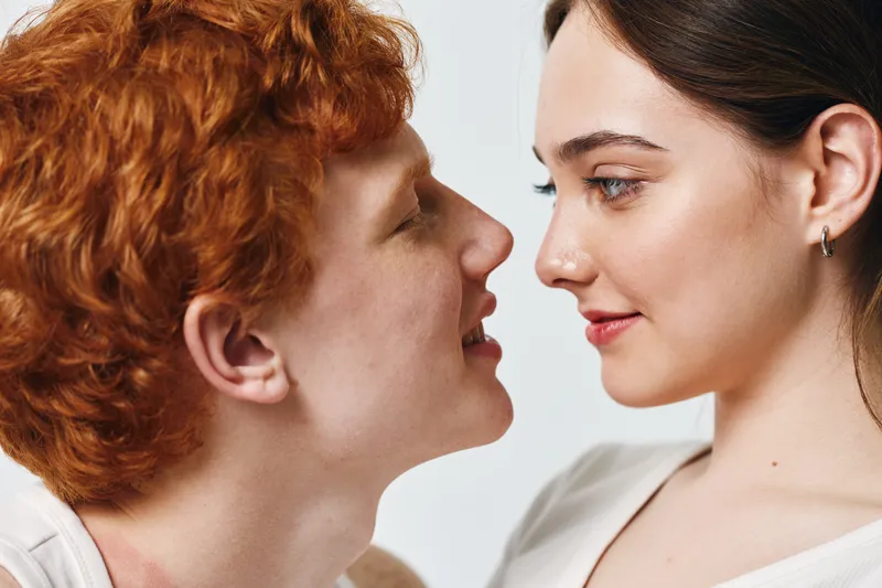 Young couple closeup with red hair man and brunette woman looking at each other, intimacy and connection in studio with light background for love and relationship.
