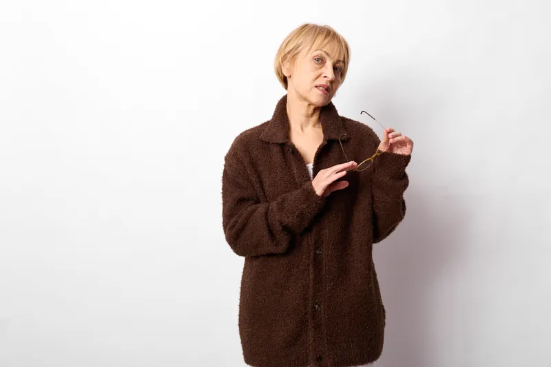 woman elderly coat jacket brown studio portrait adjusting collar cold, calm face adjusting coat in minimal studio on white background, winter fashion