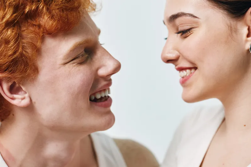 Young man and woman smiling and looking at each other with joy and happiness in closeup portrait on light background. Positive emotion and friendship concept.