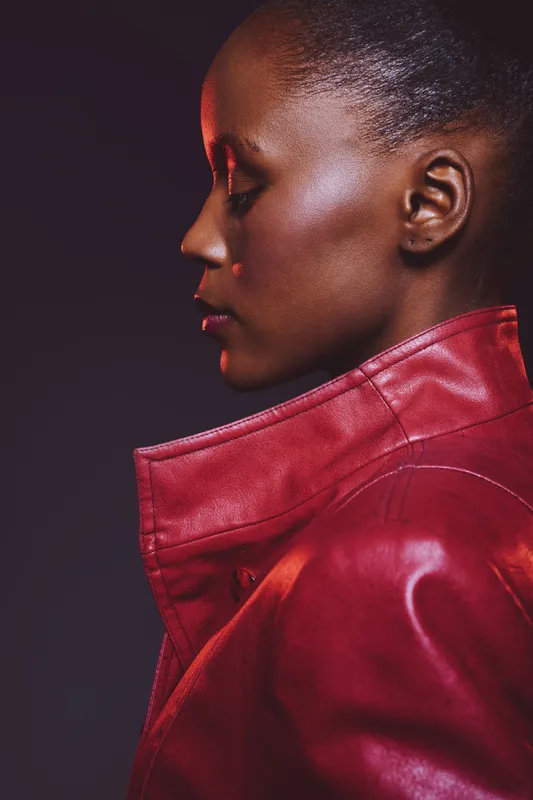 Profile of a dark skinned African woman wearing a red leather jacket against a dark background. Concept of fashion, beauty, elegance, and confident female portrait in studio lighting.