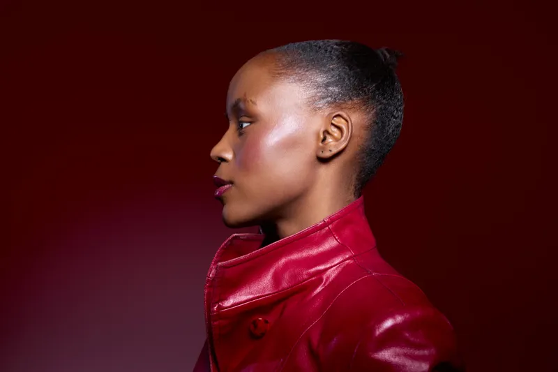 Profile of an elegant dark skinned African woman wearing a red leather jacket against a deep red background. Concept of fashion, beauty, confidence, and style in studio lighting.