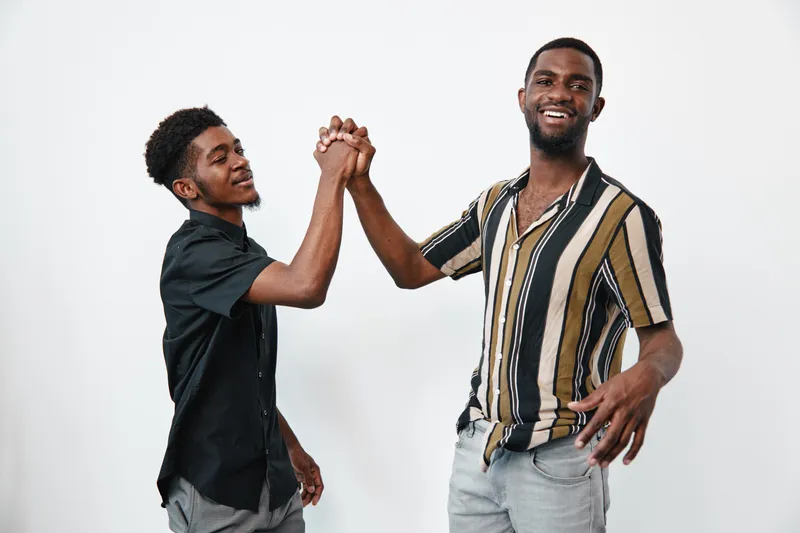 Two African American men with dark skin smiling and greeting each other with a handshake in casual clothes on white background. Friendship, connection and positive energy.