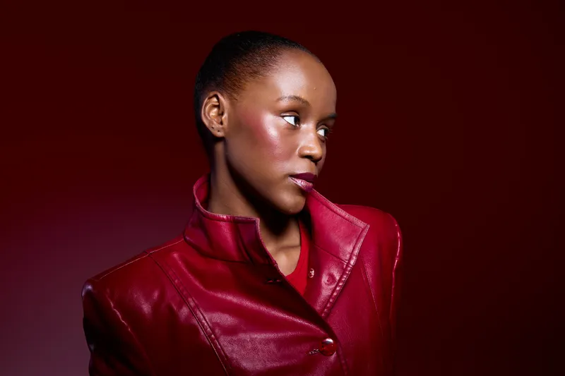 Portrait of a dark skinned African woman wearing a red leather jacket looking sideways on a red background. Concept of fashion, style, confidence, and beauty in studio lighting.