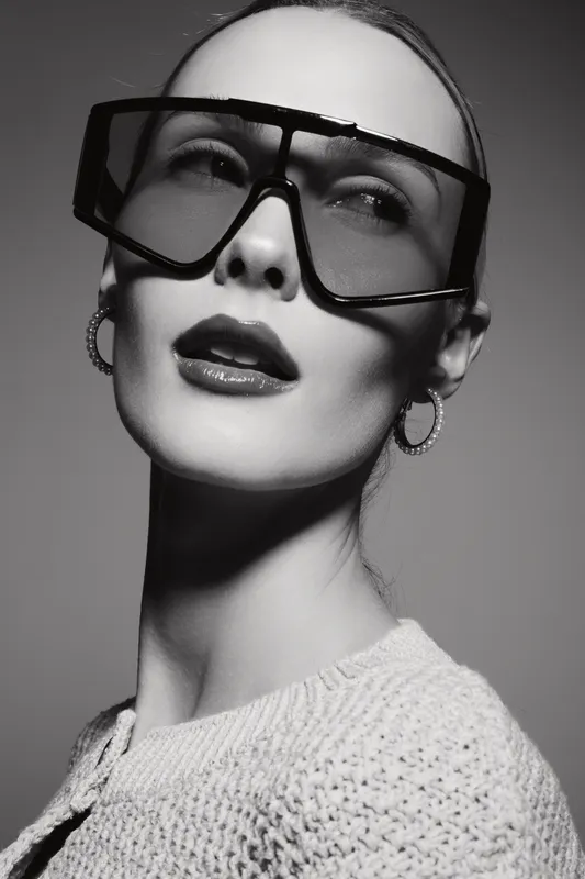 Portrait of a fair skinned Caucasian woman wearing oversized sunglasses and hoop earrings in black and white studio lighting.