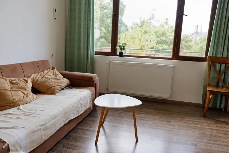 Cozy living room with a beige sofa, round white coffee table, and large window letting in soft daylight creates a calm, minimalistic home mood.
