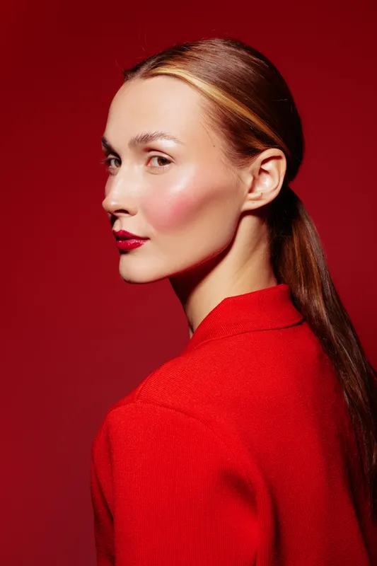 Profile of a young woman with red lipstick and blush wearing a red sweater against a red background. Concept of beauty, fashion, and confident female portrait.