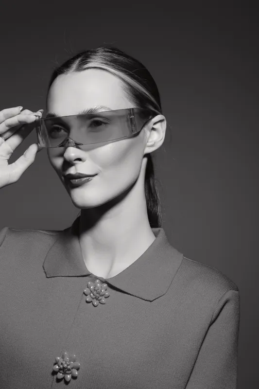 Caucasian woman with light skin wearing futuristic sunglasses and retro style clothes poses on grey background. Concept for fashion, style and modern eyewear.