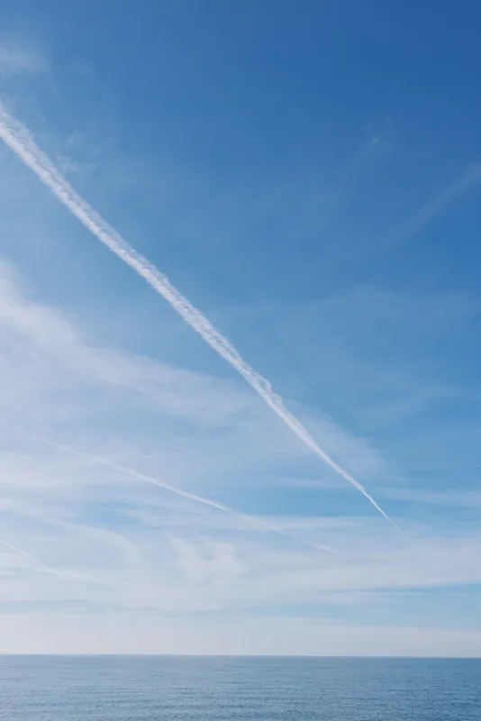 Blue sky over calm ocean with a distant horizon and white contrail. Expansive seascape conveying serenity, open air, travel mood, peaceful weather and timeless calm suitable for stock photography and