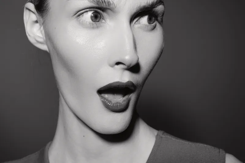 Surprised caucasian woman with pale skin and red lips looks sideways with open mouth on dark background in black and white photography.