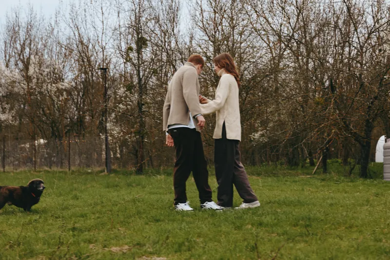 A couple walk in a park with a curious dog, sharing a quiet moment outdoors, showing lifestyle, companionship, and harmony in a natural, open setting for a wholesome mood of everyday life today.