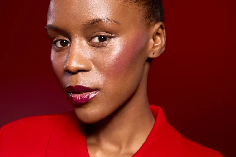 Close-up portrait of a confident black woman with dark skin wearing red clothing against a red background. The image highlights beauty, fashion, and elegance concepts.