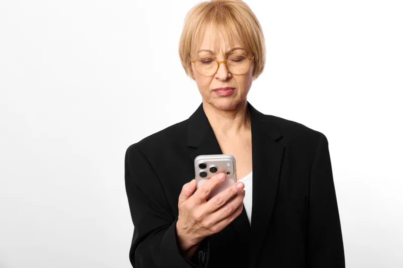 Stressed business woman in blazer, holding a smartphone with worried expression, eyes down, shoulders tensed, concept of work pressure, mental health support today