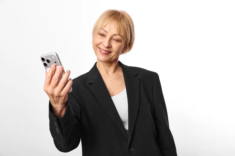 Senior woman in black blazer smile while holding smartphone for communication, business technology concept, portrait on white isolated background, copy space