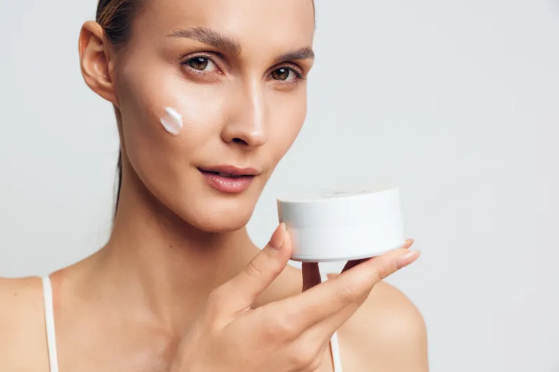 Closeup of a woman applying facial cream, skincare routine in progress, natural light, soft textures, calm expression, moisturizer ready for application on skin, radiant look and glow