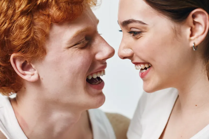 Young man and woman laughing closely together with happy faces in casual clothing on white background in studio. Intimate joyful moment with smiling emotions in friendship or love.
