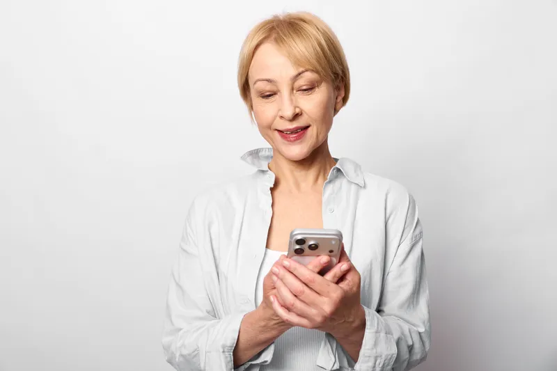 Woman senior smartphone communication texting screen portrait white studio, white background, indoor portrait with soft light, technology focus, calm expression