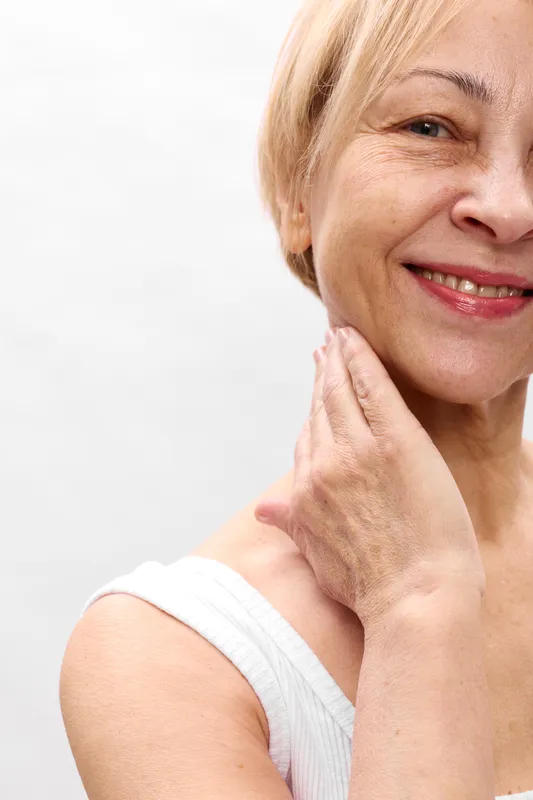 Smiling elderly woman portrait closeup, applying cream to face in skincare routine, beauty and happy wellness concept, natural white background, gentle soft studio light