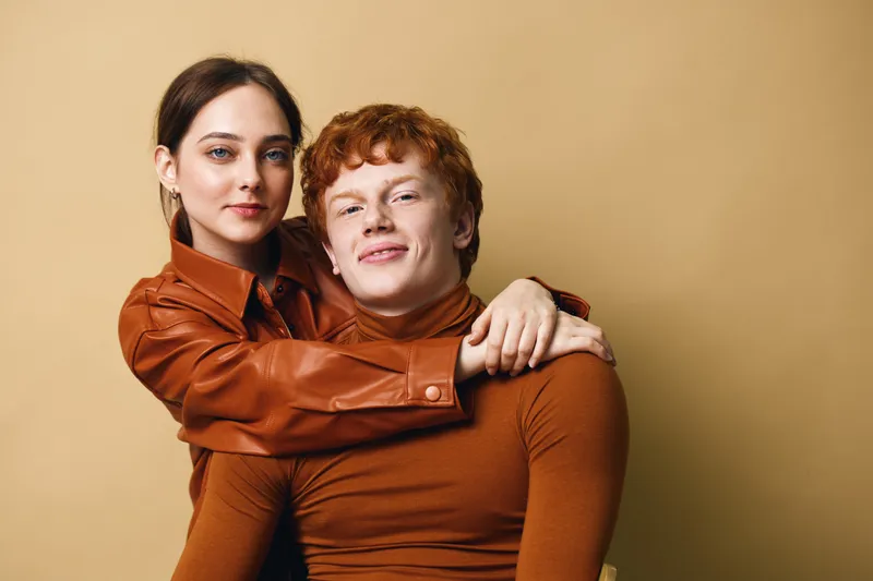 Couple, woman and man posing together smiling with warm brown outfits against beige background for love relationship and friendship closeup portrait.