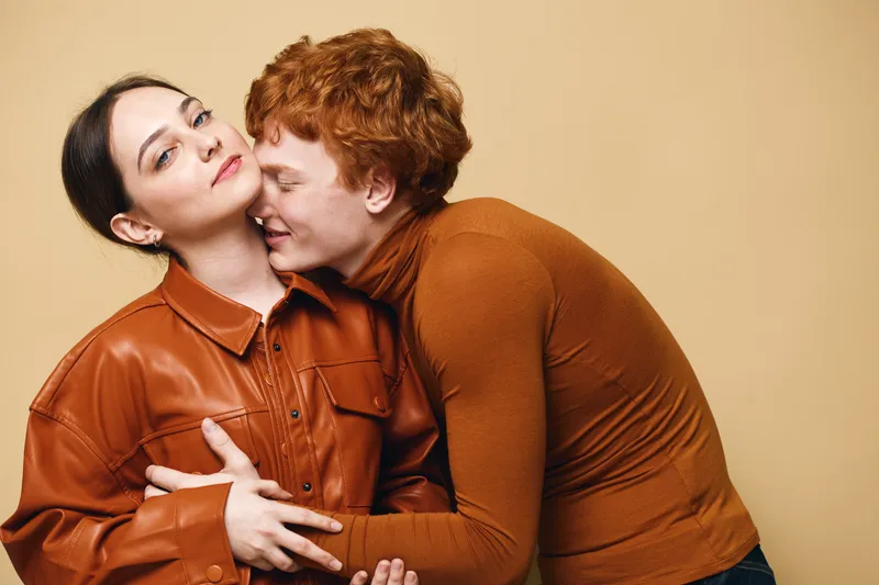 Couple, love and affection with hug and smile for relationship and intimacy in studio. Man and woman wearing brown clothes embracing with close connection and happy expression on beige background.