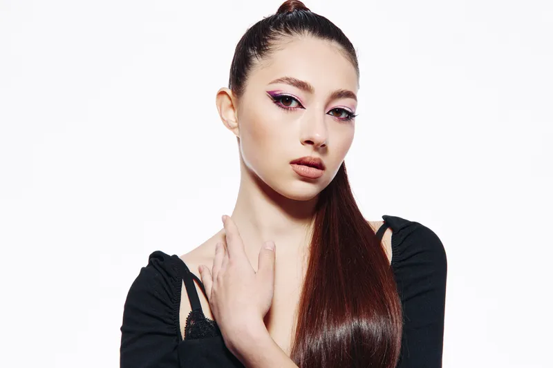 Attractive fashionable woman with long straight hair and dramatic pink eye makeup wearing black stylish top. White studio background. Creative beauty portrait for fashion concept.