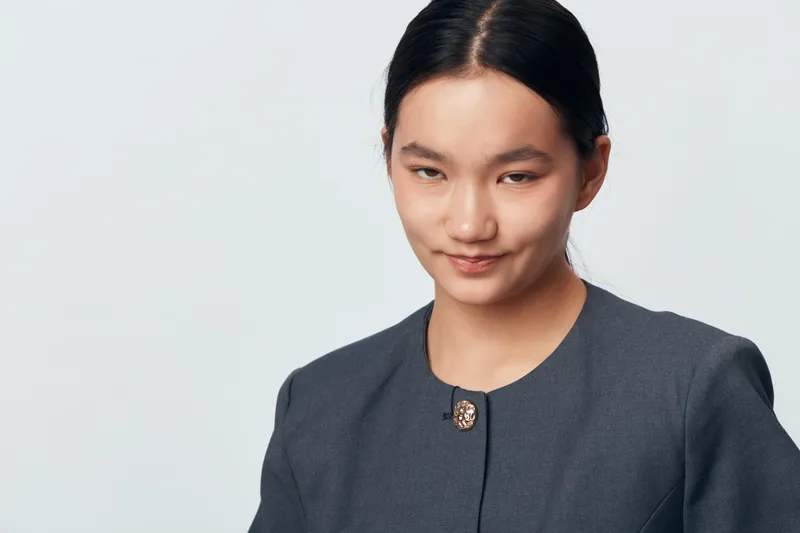 Young Asian woman with black hair in dark jacket smiling confidently on light background. Portrait of professional female with clear skin and neat hairstyle in studio.