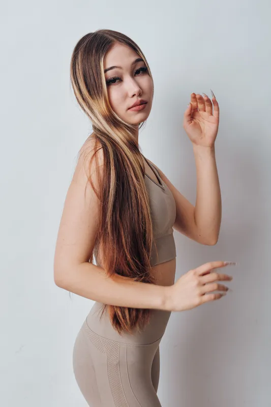 Young woman with long hair wearing beige sportswear posing against white background, fitness and beauty concept with casual lifestyle and healthy appearance.