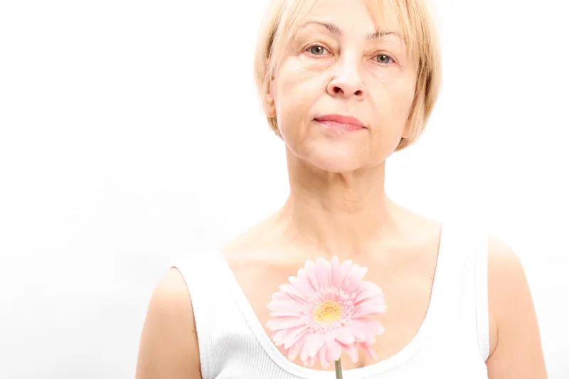Blonde woman portrait holding pink gerbera flower, older senior studio headshot on white background, calm gentle smile, beauty concept, soft light, copy space