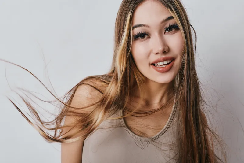 Young woman with long hair smiling and looking at camera in casual top against plain light background for beauty and portrait photography.