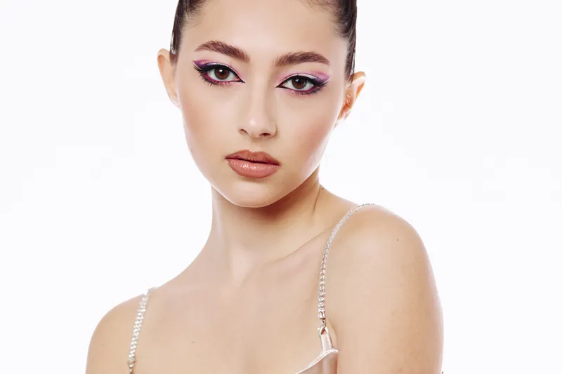 Young woman in creative fashion makeup and glitter eye shadow looks directly into the camera. Clean white background enhances the beauty aesthetic and modern look.