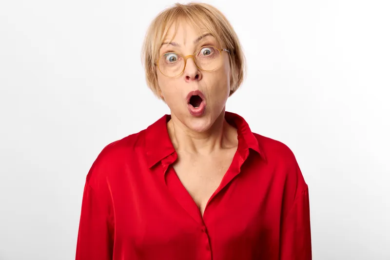 Woman wearing glasses in a red shirt, surprised with open mouth and wide eyes. Studio shot on white background. Expression of astonishment, shock, surprise, emotion.