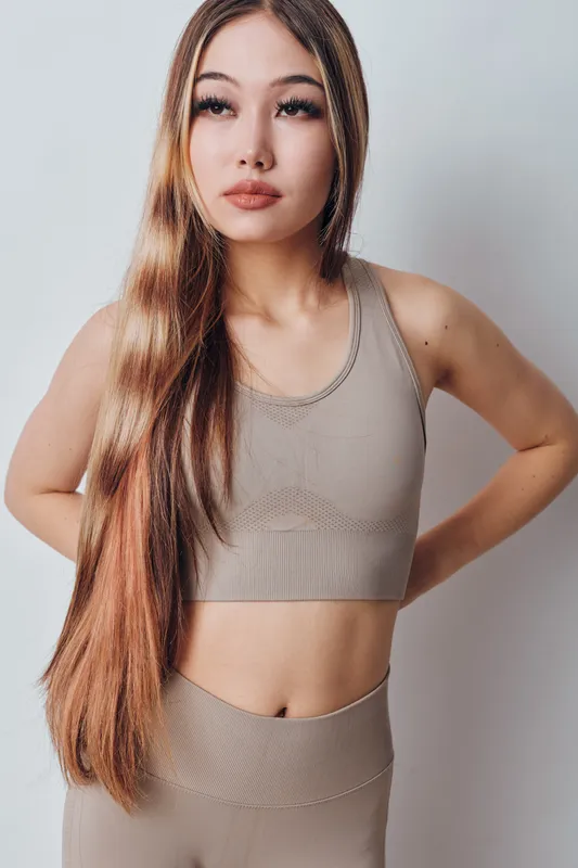 Young woman in beige sportswear standing against white background with long hair and confident expression, fitness lifestyle, health and wellness concept.