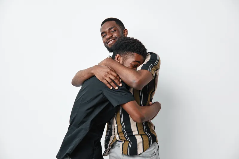 Two young black men with dark skin hugging each other in casual clothes on white background. Friends, brothers or family showing affection and emotional connection with smile and warmth.