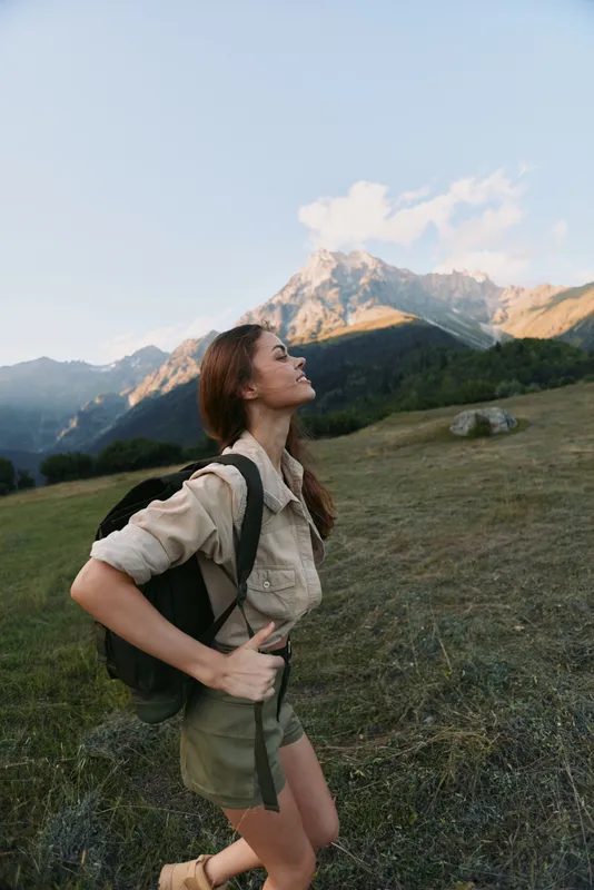 Active woman hiking outdoors with backpack in alpine meadow, mountains in the background. Adventure, nature, wellness, and outdoor lifestyle for motivation and balance.