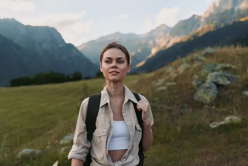 Young woman with backpack hiking in mountains enjoys nature and fresh air during outdoor adventure, wearing casual clothes and looking confident on trail.