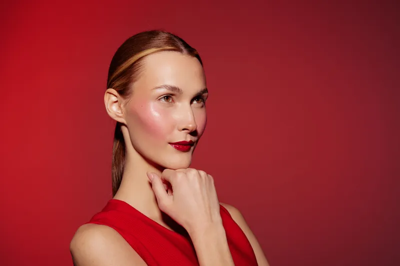 Portrait of a confident woman with red lipstick and red dress posing against a red background. Concept of beauty, fashion, elegance, and bold style in studio lighting.