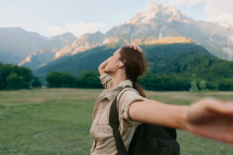 Woman outdoors with mountains backdrop, backpack ready, embraces freedom and adventure, expressing joy in a scenic landscape with nature calm, hiking inspired energy