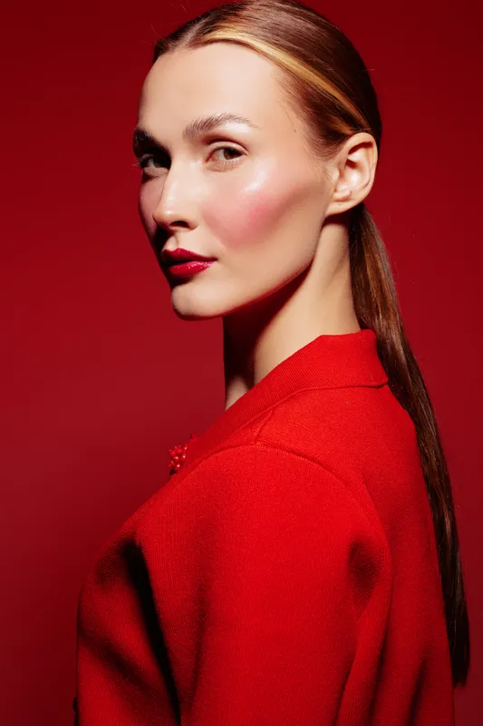 Portrait of a woman with sleek hair and red lipstick wearing a red textured jacket against a red background. Concept of fashion, beauty, elegance, and confident style.