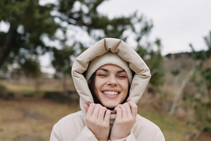 Smiling woman in a warm hooded coat outdoors in nature, close portrait with soft natural light and cozy winter mood, carefree and relaxed moment captured outside.