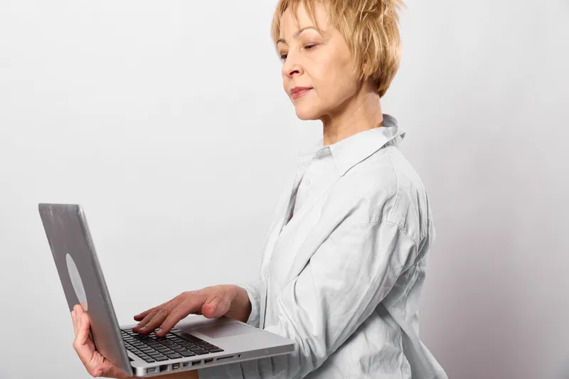 A woman in a white medical coat, a healthcare nurse types on a laptop in a bright studio, focused and calm, showing telemedicine, remote working, and communication using technology.